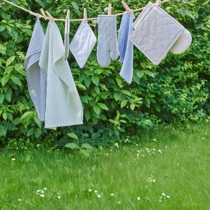Forskellige køkkentekstiler i blå/hvide nuancer hænger til tørre på snor udendørs