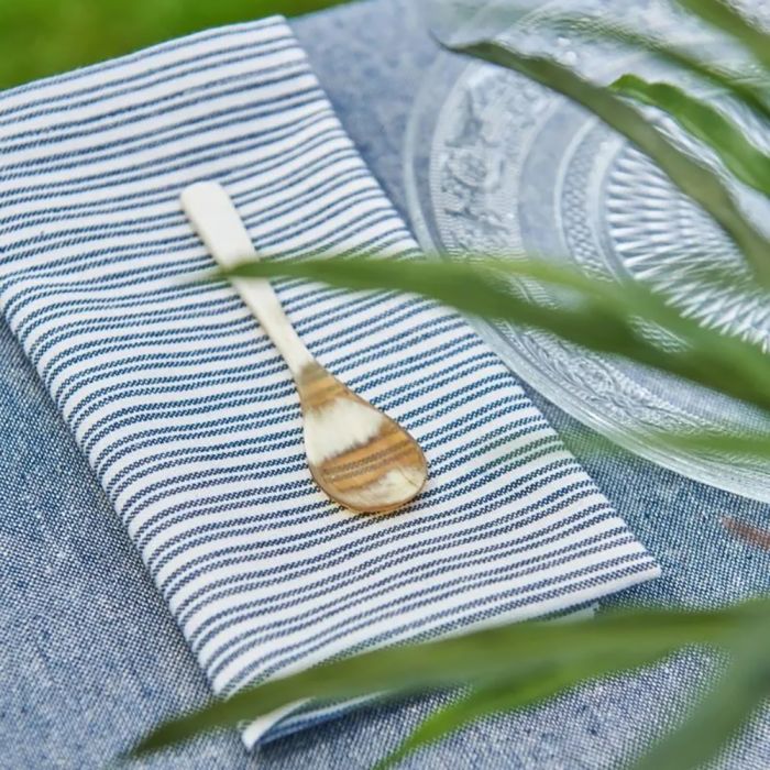 Speedtsberg stofserviet med mørkeblå striber foldet med en guldske ovenpå