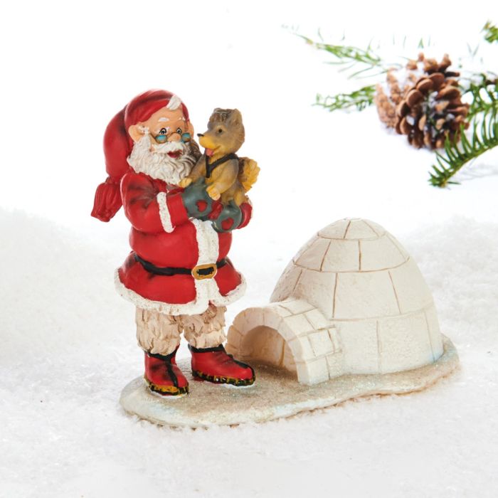 Julemand står på en isflage med iglo. Han bærer en slædehundehvalp i armene. Julemanden ser klog og glad ud, fra Pobra.