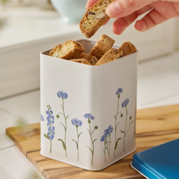 En person tager en småkage fra Ib Laursen kagedåse med blå kornblomster