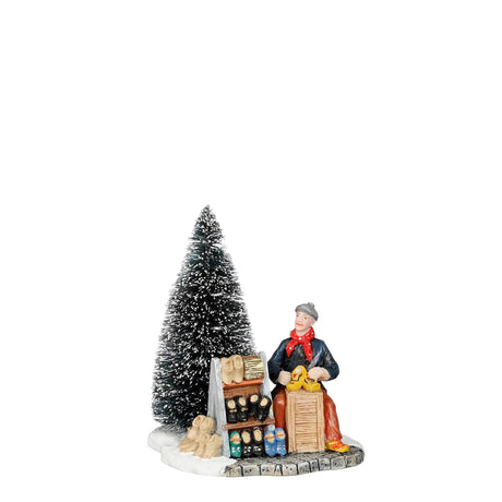 Miniature figur med træskobod og juletræ i baggrunden