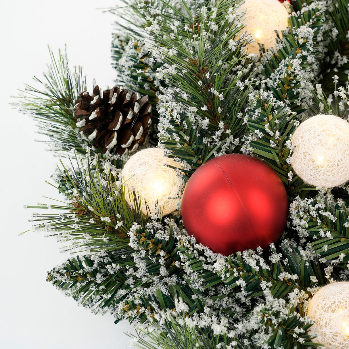 Rød julekugle, kogle og lysende bolde på krans