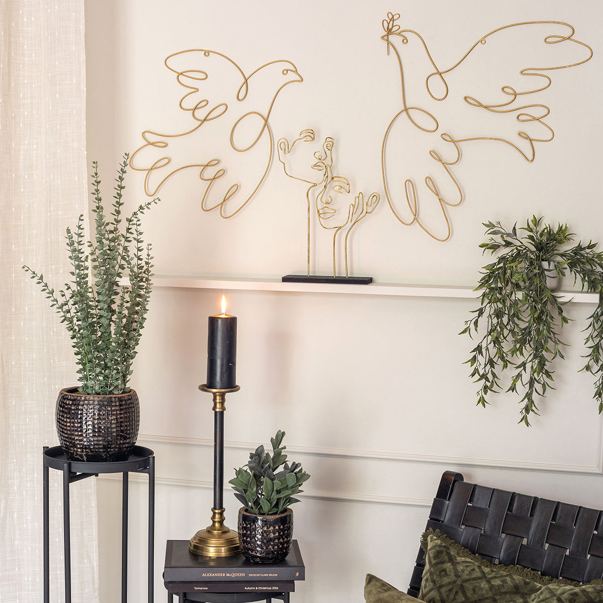 Væg med guldfarvet vægdekorationer i metal samt hyggehjørne med sidebord og lænestol