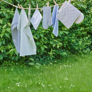 Forskellige køkkentekstiler i blå/hvide nuancer hænger til tørre på snor udendørs