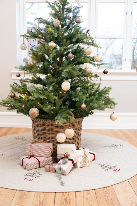 Juletræ med pynt i kurv stående på juletræstæppet quiltet med broderi