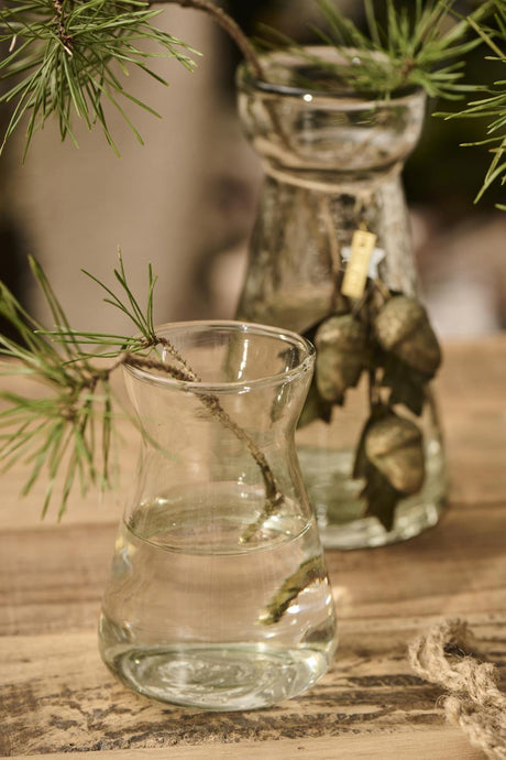 Hyacintvase fra Ib Laursen med grønne grene som vinterdekoration på et rustikt bord