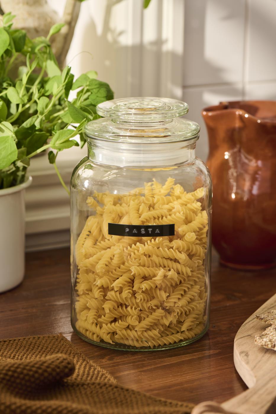 Opbevaringsglas med låg fyldt med pasta på et rustikt køkkenbord