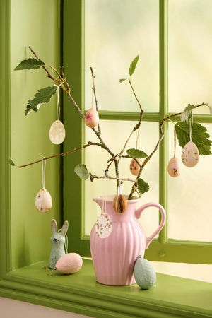 Kande med grene pyntet med påskeæg stående i vindueskarm