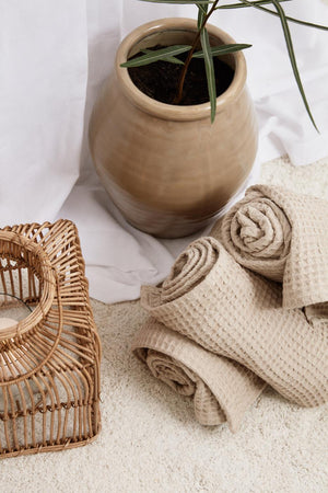 Sammenfoldede beige Liseleje håndklæder ved en lille plante og kurv i naturlige materialer