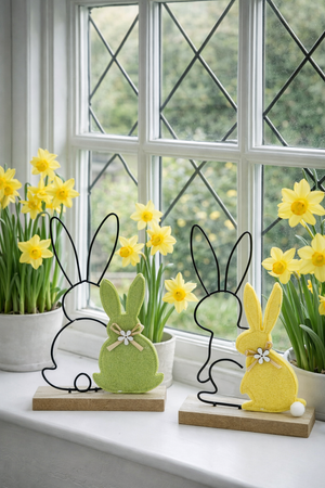 Påskehare i filt med haresilhuet sammen med påskeliljer i en vindueskarm